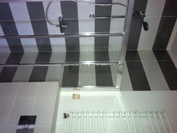 kabina prysznicowa, na scianie pasy ulozone z kafelkow czarnych i bialych, dodatkowo przy toalecie kafelki jasnoszare